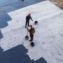 To arbeidere smører flytende asfalt på tak